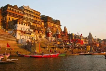 People walking along stone steps beside the river during the day, with boats on the water and historic buildings in the background.